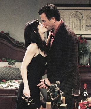 Monica embrasse Richard. Elle porte une slip dress noire. 
